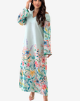 A woman modeling a long, off-the-shoulder maxi dress with a light mint green base and a vibrant multicolor floral print on the sleeves and lower skirt, set against a plain light gray background.