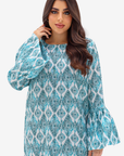 A woman modeling a long-sleeve tunic dress with a blue and white geometric pattern, set against a plain light gray background.