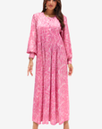 A woman modeling a long-sleeved pink maxi dress with a white abstract pattern, shown against a plain light gray background.