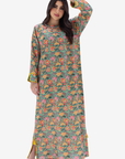 A woman modeling a long-sleeved, floor-length kurta with a dense floral and botanical print in green, pink, orange, and yellow, set against a plain light gray background.
