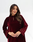 Three-quarter portrait of burgundy velvet jalabiya showing the embroidered sleeve cuffs