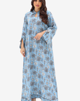 A woman modeling a light blue maxi dress with a gray and beige palm tree pattern, set against a plain light gray background.