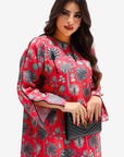 A woman modeling a red long-sleeve tunic dress with a black and gray palm tree pattern, holding a black quilted clutch bag against a light gray background.