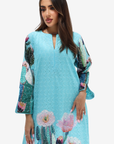 A woman modeling a light blue eyelet kaftan dress with a colorful cactus and flower print on the sleeves and hem, set against a plain white background.