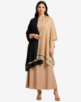A woman modeling a draped beige and black shawl with a geometric patterned border over a beige maxi dress, set against a plain light gray background.