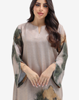 A woman modeling a loose, long-sleeved tunic dress with a beige base and green, brown, and gold abstract watercolor-style print on the sleeves and hem, set against a plain light gray background.