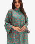 A woman modeling a long-sleeved high-neck tunic dress with a vibrant green, red, and orange mandala pattern against a light gray studio background.