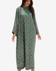 A woman modeling a long-sleeve, high-neck maxi dress with a colorful geometric and floral pattern in teal, orange, and green, set against a plain light gray background.