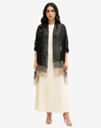A woman modeling a black sheer open-front cardigan with beige lace trim over a cream maxi dress, standing against a light gray studio background.