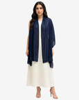 A woman modeling a navy blue shawl with geometric embroidered detailing down the center, worn over a white maxi dress against a light gray background.