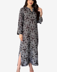 A woman modeling a long-sleeved, floor-length kaftan dress with a gray and black geometric peace-sign pattern, shown against a plain light gray background.