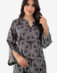 A woman modeling a black long-sleeve tunic with a white geometric interlocking pattern and white piping details on the neckline and cuffs, set against a plain light gray background.