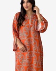 A woman modeling a long-sleeved orange kaftan dress with a beige geometric interlocking pattern, featuring a split neckline with white drawstrings and flared bell sleeves with white piping.