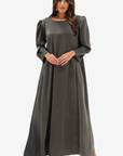 A woman modeling a long, flowing dark olive green dress with long puff sleeves and a round neckline, standing against a plain light gray background.