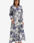 A woman modeling a long-sleeved maxi dress with a blue and white palm tree pattern, paired with a matching headband and nude high-heeled sandals, set against a plain light gray background.