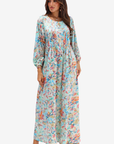 A woman modeling a long-sleeve maxi dress with a colorful abstract floral print on a light mint green background, paired with pink strappy heels, against a plain white studio background.