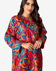 A woman wearing a long-sleeve collared button-front dress with a bold abstract wavy pattern in red, orange, blue, and yellow, photographed against a light gray studio background.