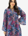 A woman modeling a long-sleeved bohemian-style tunic dress with a vibrant floral print in shades of purple, blue, and orange, featuring a lace-up neckline.