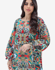 A woman modeling a long-sleeved, loose-fitting tunic dress with a vibrant, multicolor abstract pattern on a light gray background.