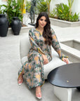 Woman in a patterned dress sitting on a white chair with plants in the background