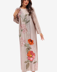 A woman modeling a long, loose-fitting beige maxi dress with pink and orange floral embroidery and sequin detailing, set against a plain light gray background.