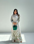 Woman wearing a long floral dress with a green handbag on a white background