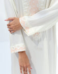 Close-up of a person's hands holding a white fabric with floral embroidery on a white background