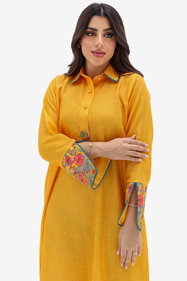A woman modeling a mustard yellow long-sleeve kurta with colorful floral embroidery on the cuffs and collar, set against a plain light gray background.