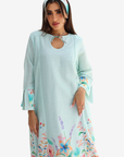 A woman modeling a light mint green maxi dress with a colorful floral print at the hem and cuffs, paired with a matching floral headband, against a plain white background.