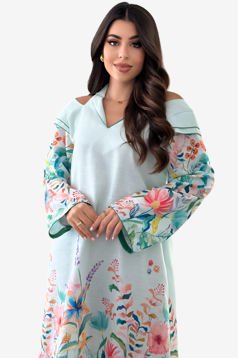 A woman modeling a light blue off-the-shoulder tunic dress with vibrant multicolor floral patterns on the sleeves and hem, set against a plain light gray background.