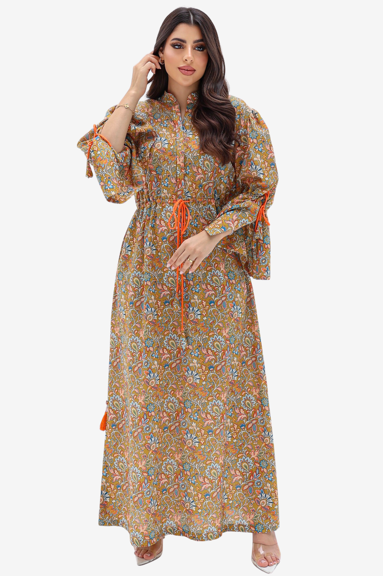 A woman modeling a long-sleeved, ankle-length floral maxi dress with a brown base and orange tie details, set against a plain light gray background.