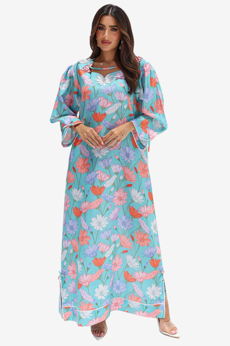 A woman modeling a long, flowing maxi dress with a vibrant floral print on a light turquoise background. The dress features wide, balloon sleeves, a V-neckline with a small keyhole cutout detail, and a side slit at the hem.