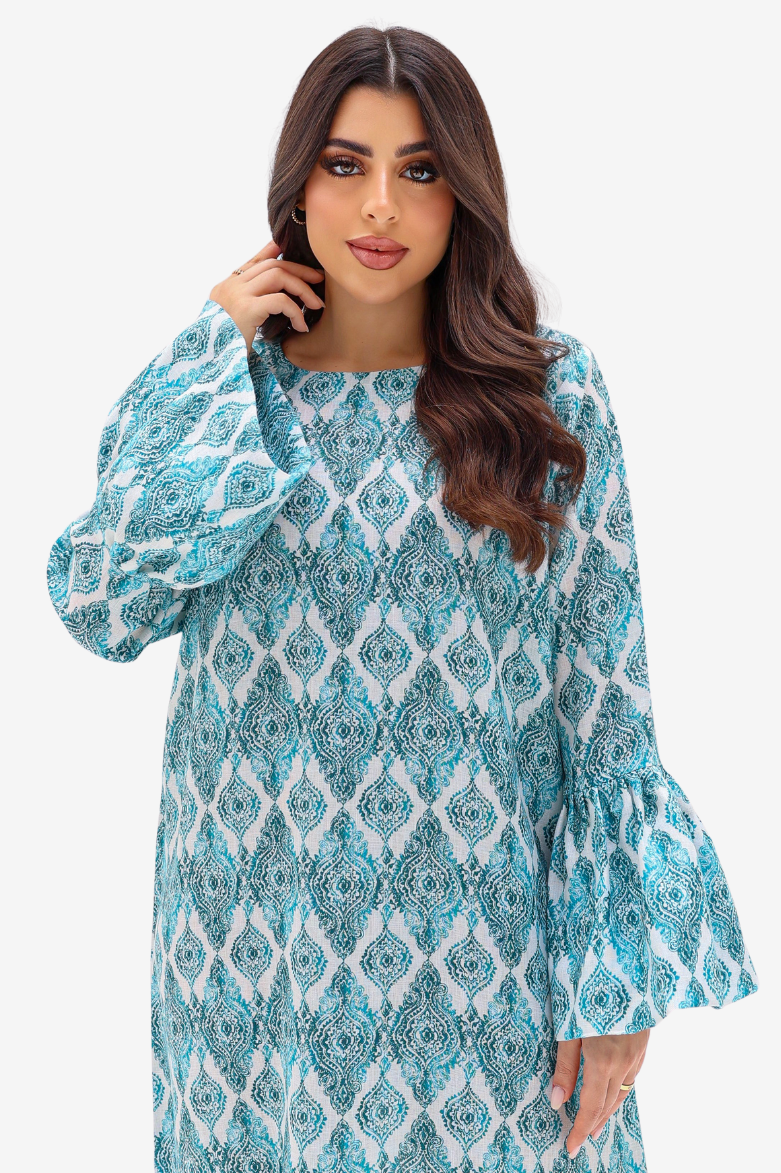 A woman modeling a long-sleeve tunic dress with a blue and white geometric pattern, set against a plain light gray background.