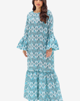 A woman modeling a long-sleeved maxi dress with a blue and white geometric pattern, flared bell sleeves, and a tiered ruffled hem against a light gray background.