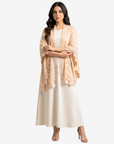 A woman modeling a light peach-beige open-front shawl or lightweight jacket with floral lace trim over a cream dress, photographed against a plain light gray studio background.
