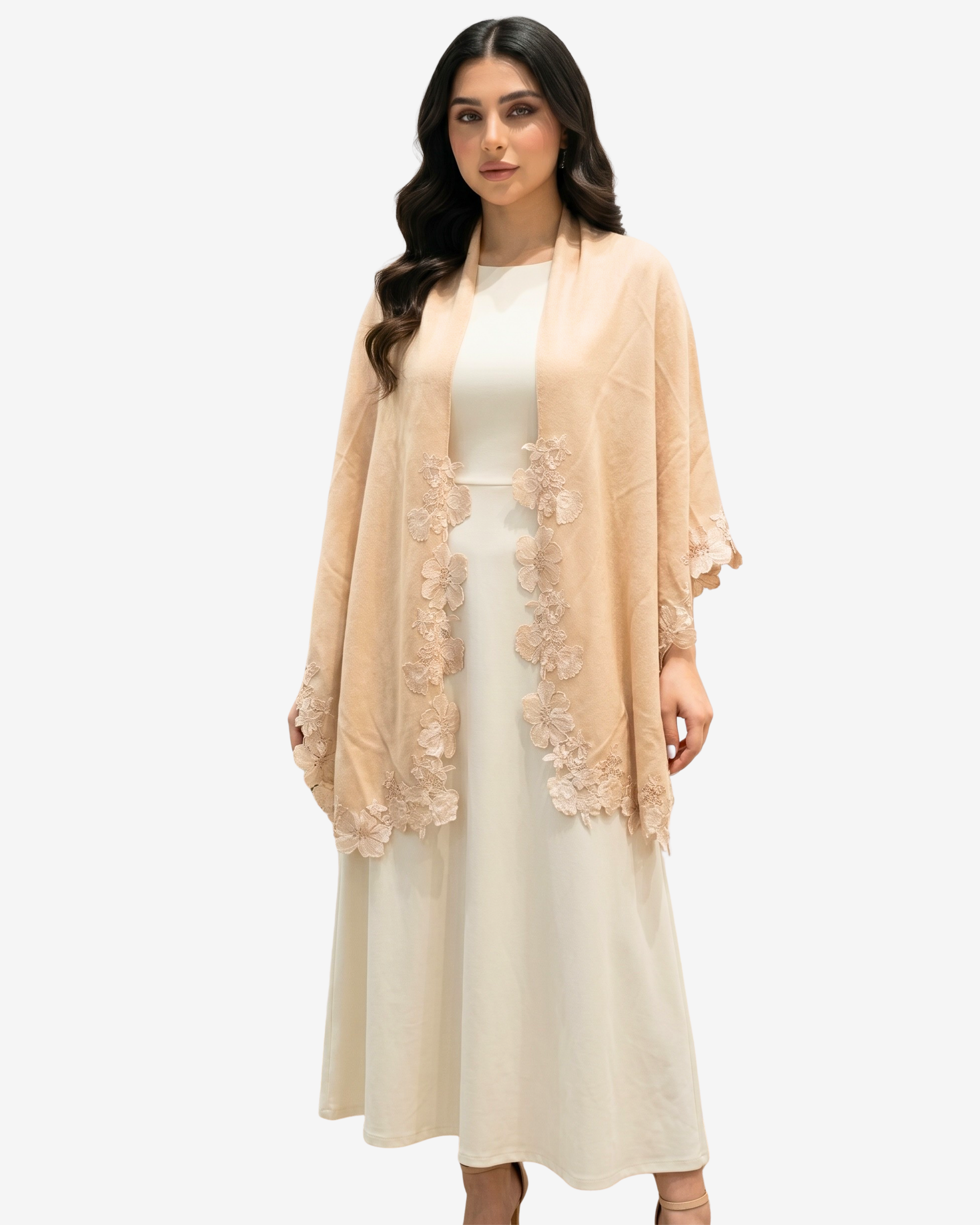 A woman modeling a light peach-beige open-front shawl or wrap with floral lace trim over a cream midi dress, set against a plain light gray studio background.