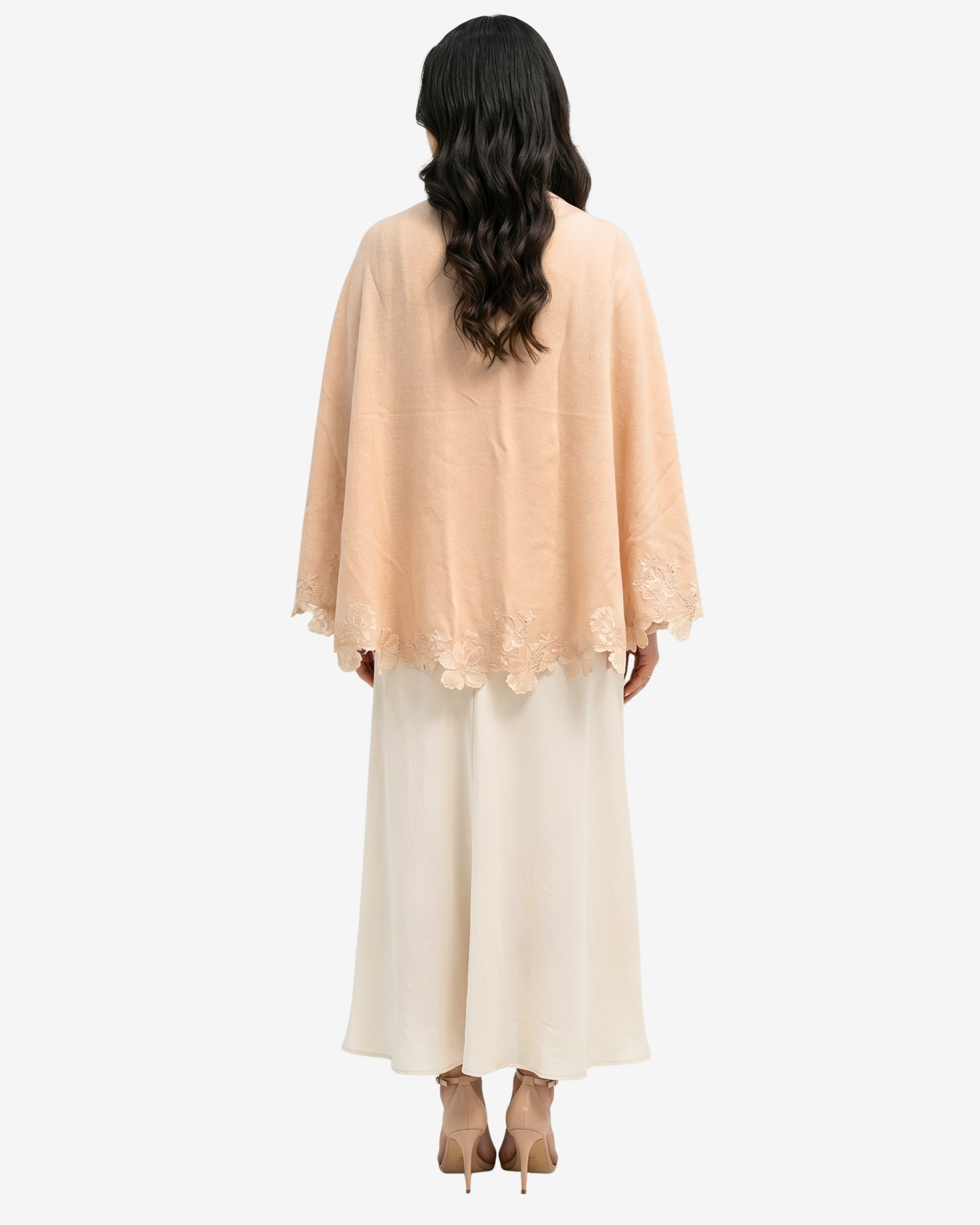 A woman shown from the back wearing a peach-colored lace-trimmed cape-style top over a long cream dress, against a plain light gray background.