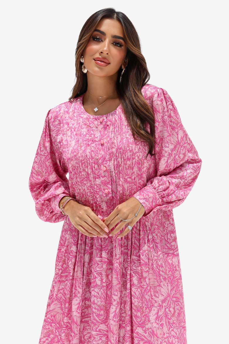A woman modeling a pink long-sleeve dress with a white abstract floral print, featuring a buttoned neckline and a gathered, flowing skirt, set against a plain light gray background.