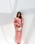 Woman in a pink floral dress holding a white clutch against a white background