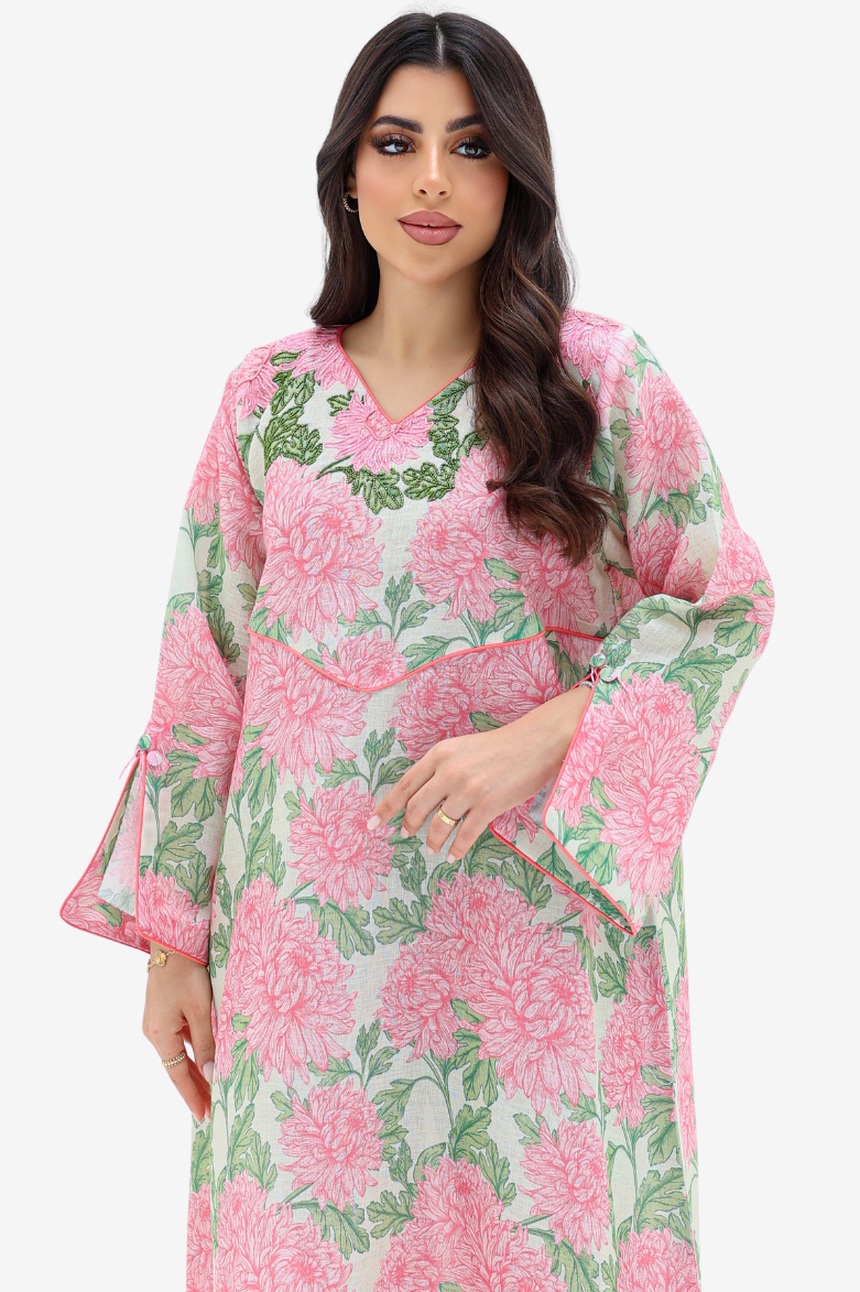 A woman modeling a long-sleeve kaftan dress with a pink and green floral print on a light background, set against a plain light gray studio backdrop.
