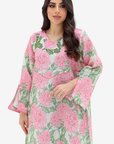 A woman modeling a long-sleeve kaftan dress with a pink and green floral print on a light background, set against a plain light gray studio backdrop.