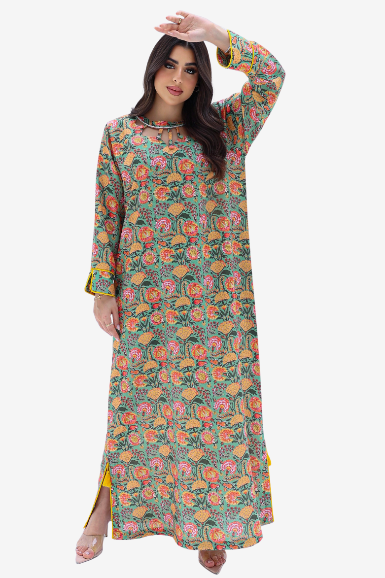 A woman modeling a long-sleeved, floor-length kurta with a dense floral and botanical print in green, pink, orange, and yellow, set against a plain light gray background.