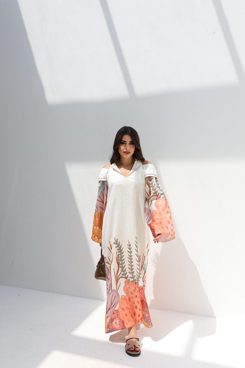 Woman wearing a long, light-colored dress with floral patterns in a minimalistic setting.
