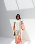 Woman wearing a long, light-colored dress with floral patterns in a minimalistic setting.