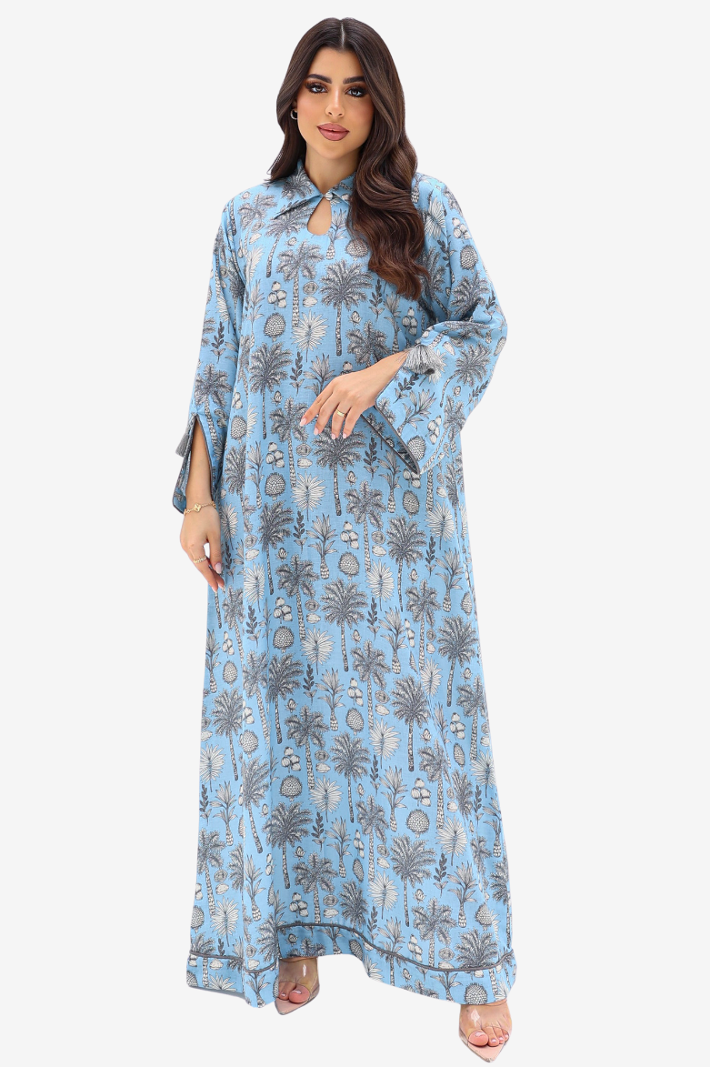 A woman modeling a light blue maxi dress with a gray and beige palm tree pattern, set against a plain light gray background.
