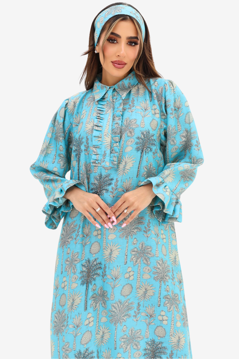 A woman wearing a light blue long-sleeve abaya dress with a gray palm tree pattern, paired with a matching headband, against a plain light gray background.