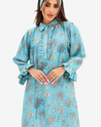 A woman wearing a light blue long-sleeve abaya dress with a gray palm tree pattern, paired with a matching headband, against a plain light gray background.