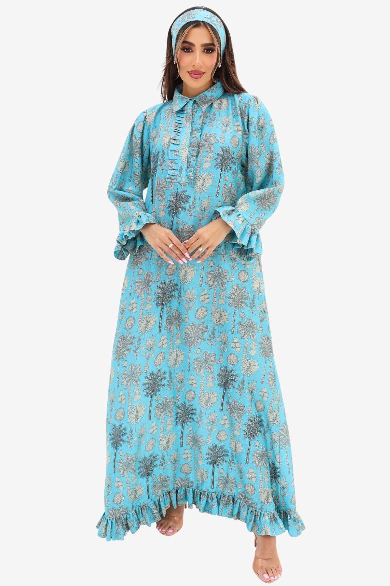 A woman modeling a long-sleeved, high-neck maxi dress in light blue with a gray palm tree and circular pattern, paired with a matching headband, against a plain light gray background.