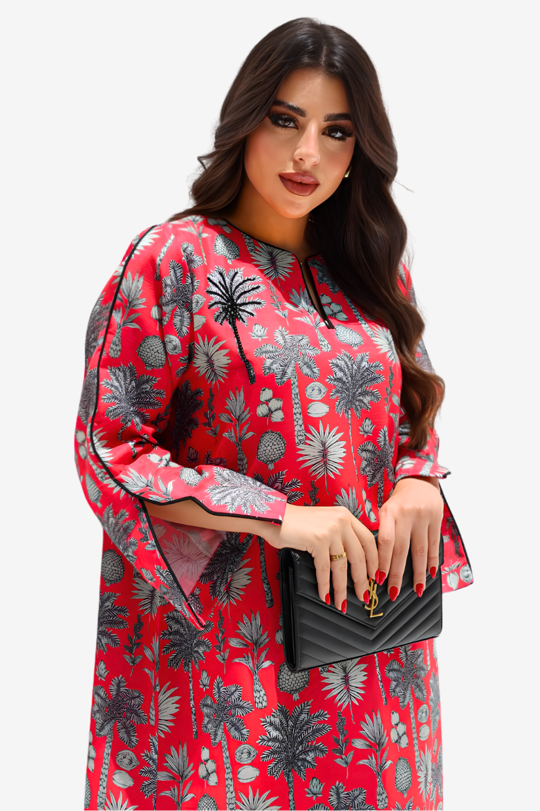 A woman modeling a red long-sleeve tunic dress with a black and gray palm tree pattern, holding a black quilted clutch bag against a light gray background.