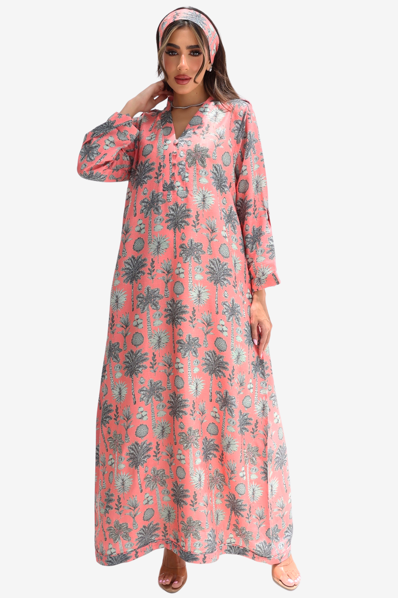 A woman modeling a long-sleeved, floor-length pink kaftan dress with a gray palm tree and circular pattern, paired with a matching pink and gray headscarf, set against a plain light gray background.